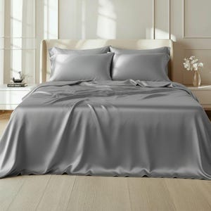 May include: A bed is made with a gray silk sheet set. The set includes a fitted sheet, a flat sheet, and two pillowcases. The sheets have a lustrous sheen and are neatly arranged on the bed, creating a luxurious and inviting look.