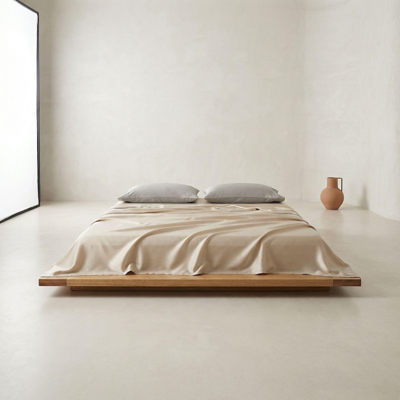 May include: A low-profile wooden bed frame with a beige sheet and two gray pillows. A terracotta vase sits in the background. The bed is the focal point, showcasing a minimalist design.