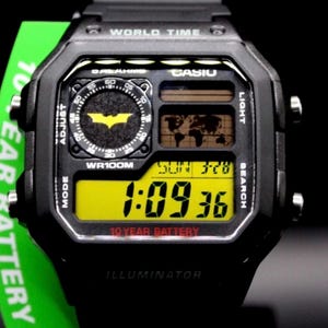 May include: Black Casio digital watch with a Batman logo on the face. The watch displays the time, date, and world map. The watch has a yellow digital display and the text "10 YEAR BATTERY".