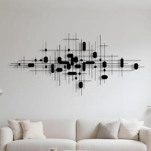 Può includere: Opera d'arte da parete astratta in metallo nero con un design di linee e forme ovali che si intersecano. L'opera è montata su una parete bianca sopra un divano color crema, creando un'estetica moderna e minimalista. Il pezzo aggiunge un tocco di raffinatezza al soggiorno.