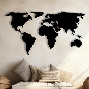 Puede incluir: Un mapa del mundo de metal negro montado en una pared crema. Los continentes del mapa son de color negro sólido, creando un contraste llamativo. La decoración de la pared está sobre una zona de estar con cojines y una base de madera.