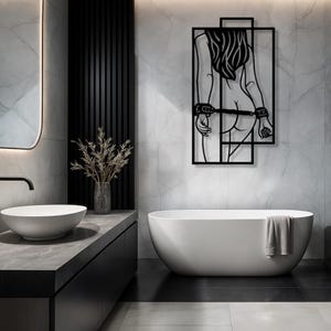 May include: Black metal wall art depicting a stylized figure with long hair, hands behind the back, and handcuffs. The artwork is set against a marble-patterned wall in a modern bathroom setting, with a white bathtub and sink.
