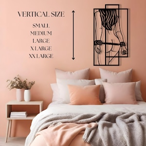 May include: A black metal wall art piece depicting a silhouette of a person with handcuffs. The artwork is mounted on a peach-colored wall above a bed with peach and white bedding. Text on the wall indicates vertical size options.