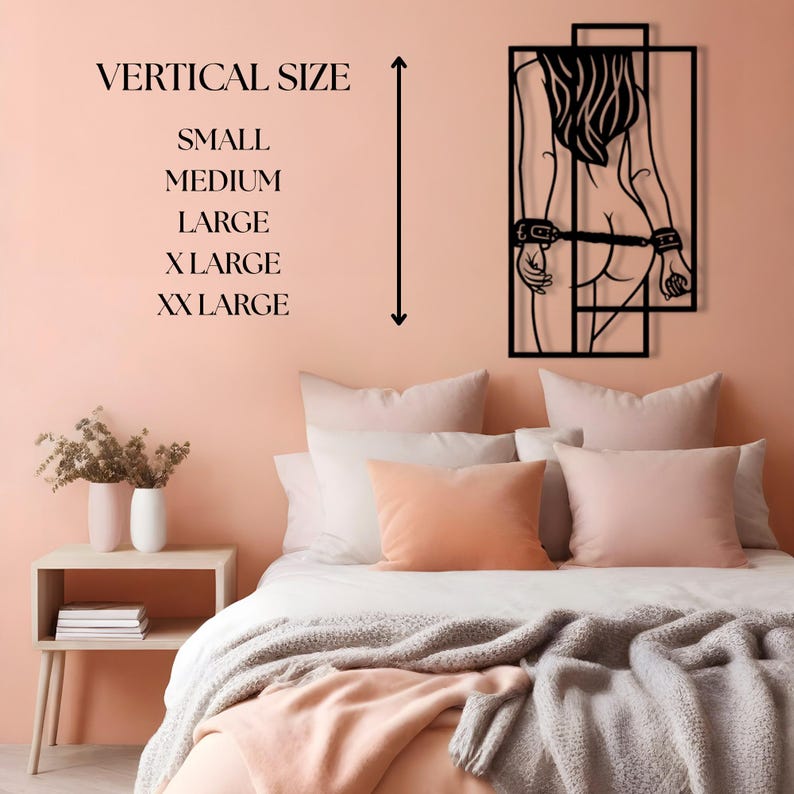 May include: A black metal wall art piece depicting a silhouette of a person with handcuffs. The artwork is mounted on a peach-colored wall above a bed with peach and white bedding. Text on the wall indicates vertical size options.