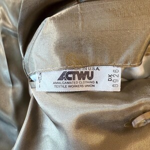 May include: Close-up of a tan garment with a tag that reads "MADE IN U.S.A." and "ACTWU AMALGAMATED CLOTHING & TEXTILE WORKERS UNION." The fabric has a subtle sheen.