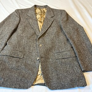 May include: A brown tweed blazer with a classic three-button closure and notched lapels. The jacket features two front pockets and a gold-colored lining. The sleeves have buttoned cuffs. This tailored jacket is suitable for formal or business attire.