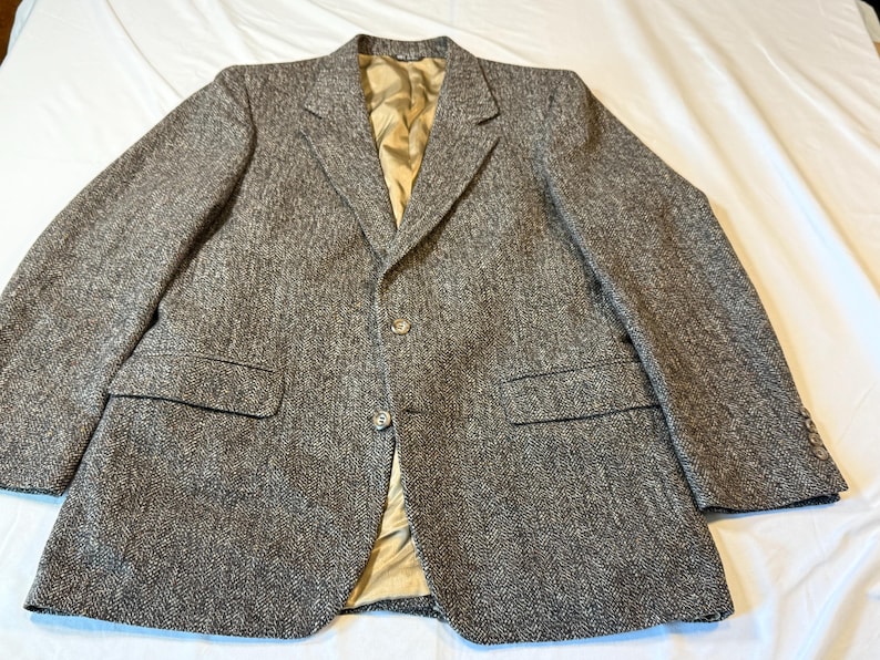 May include: A brown tweed blazer with a classic three-button closure and notched lapels. The jacket features two front pockets and a gold-colored lining. The sleeves have buttoned cuffs. This tailored jacket is suitable for formal or business attire.