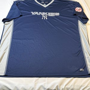 May include: Navy blue V-neck baseball jersey with the word "Yankees" in white across the chest. The jersey has a white and gray trim on the sides and a team logo patch on the left sleeve. The jersey is made of a breathable material.