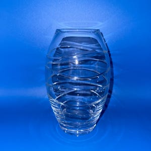 May include: A clear glass vase with a rounded, tapered silhouette featuring a series of etched, swirling horizontal lines that wrap around the exterior surface, creating a textured pattern against the transparent body of the vessel.
