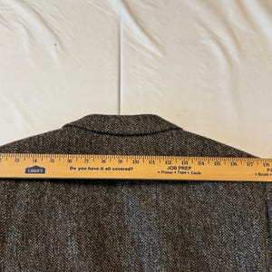 May include: A brown tweed blazer with a wooden ruler laid across the back. The ruler measures approximately 20 inches. The blazer has a herringbone pattern and a notched collar. The text "Do you have it all covered?" is visible on the ruler.
