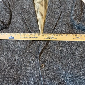 May include: A brown tweed blazer with a notched lapel and a single-button closure. The blazer has a light-colored lining and a ruler is placed across the front. The ruler reads "Do you have it all covered?" and "Job Prep".