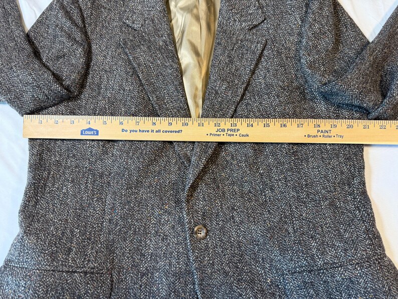 May include: A brown tweed blazer with a notched lapel and a single-button closure. The blazer has a light-colored lining and a ruler is placed across the front. The ruler reads "Do you have it all covered?" and "Job Prep".