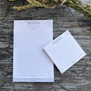 May include: Two white paper notepads with horizontal lines and floral accents. The larger pad features the text "NOTES," "Peace I leave with you," "John 14:27," "CAST ALL YOUR ANXIETY ON HIM BECAUSE HE CARES FOR YOU," and "BE STILL AND KNOW THAT I AM GOD."
