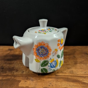 May include: A white ceramic mug with a black handle and the text "But First, Coffee" in a handwritten style. The mug is on a white surface. The mug is 4 inches tall.