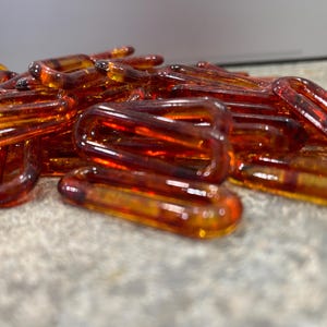 Op de afbeelding: Een verzameling doorschijnende, barnsteenkleurige plastic kettingschakels met een glanzende afwerking. De ovaalvormige schakels liggen verspreid in een hoop en vertonen een warme, honingachtige tint met subtiele variaties in kleurdiepte.
