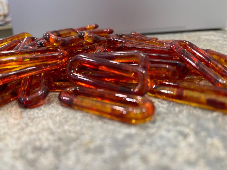Op de afbeelding: Een verzameling doorschijnende, barnsteenkleurige plastic kettingschakels met een glanzende afwerking. De ovaalvormige schakels liggen verspreid in een hoop en vertonen een warme, honingachtige tint met subtiele variaties in kleurdiepte.