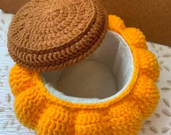 May include: A handmade crochet box with a lid. The box is pumpkin-shaped, with a bright orange exterior and a brown lid. The interior is lined with a light-colored fabric. The lid is slightly ajar, revealing the inside.