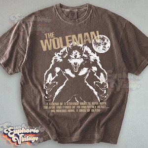 May include: Brown t-shirt featuring a white illustration of a werewolf with the text "THE WOLFMAN" and a full moon. The shirt also includes the text "A LEGEND OF A STRANGE MORTAL MAN WITH THE HAIR AND FANGS OF AN UNEARTHLY BEAST... HIS HIDEOUS HOWL A DIRGE OF DEATH-".