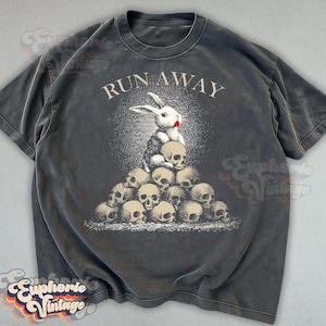 May include: Dark gray t-shirt with a graphic of a white rabbit with a red mouth sitting on a pile of skulls. The text "RUN AWAY" is arched above the rabbit. The shirt has a vintage, distressed look.