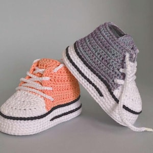 May include: Two handmade crochet baby sneakers. One is peach and white, the other is gray and white. Both have white laces, black trim, and a white sole. These adorable baby shoes are perfect for a newborn.