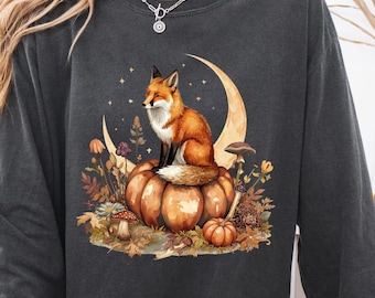 May include: Dark gray sweatshirt featuring a watercolor illustration of a fox sitting on a pumpkin in front of a crescent moon. The design includes mushrooms, flowers, and stars, with the word "Pepper" at the bottom.