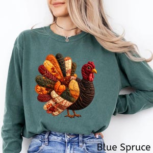 May include: Blue Spruce sweatshirt featuring a colorful turkey graphic. The turkey has a detailed design with autumn-themed feathers, a red head, and a yellow beak. The text "Blue Spruce" is at the bottom of the image.