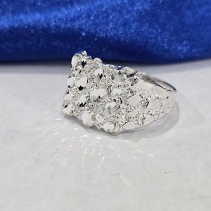 May include: A silver-toned ring featuring a textured, nugget-style design across the top surface. The metal has a high-polish finish with multiple faceted, reflective surfaces that create a bright, shimmering appearance across the entire band.