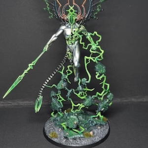 May include: A detailed miniature figure of a science fiction character. The figure is primarily silver with green energy effects, a spear, and a complex headpiece. The base is a textured gray with green accents.