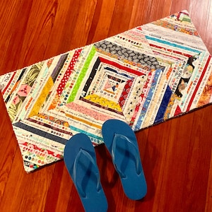 Pode incluir: Um tapete de patchwork colorido com um design geométrico. O tapete é feito de tiras de tecido em várias cores e padrões. Duas sandálias de dedo azuis estão sobre o tapete.