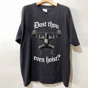 May include: Black t-shirt featuring a knight lifting a barbell, with the text "Dost thou even hoist?" in white gothic font. The knight is in full armor. The shirt is hanging on a wooden hanger.