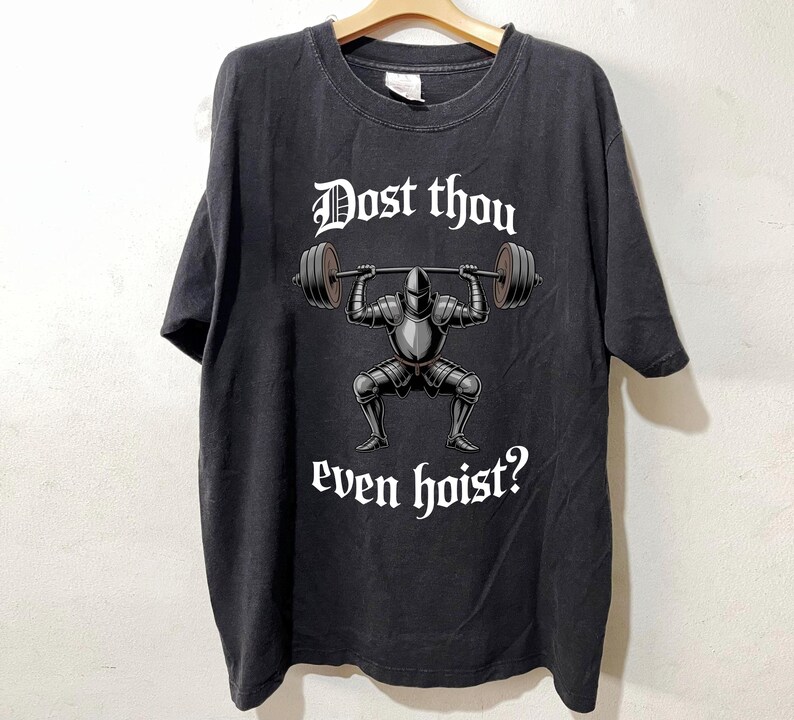 May include: Black t-shirt featuring a knight lifting a barbell, with the text "Dost thou even hoist?" in white gothic font. The knight is in full armor. The shirt is hanging on a wooden hanger.