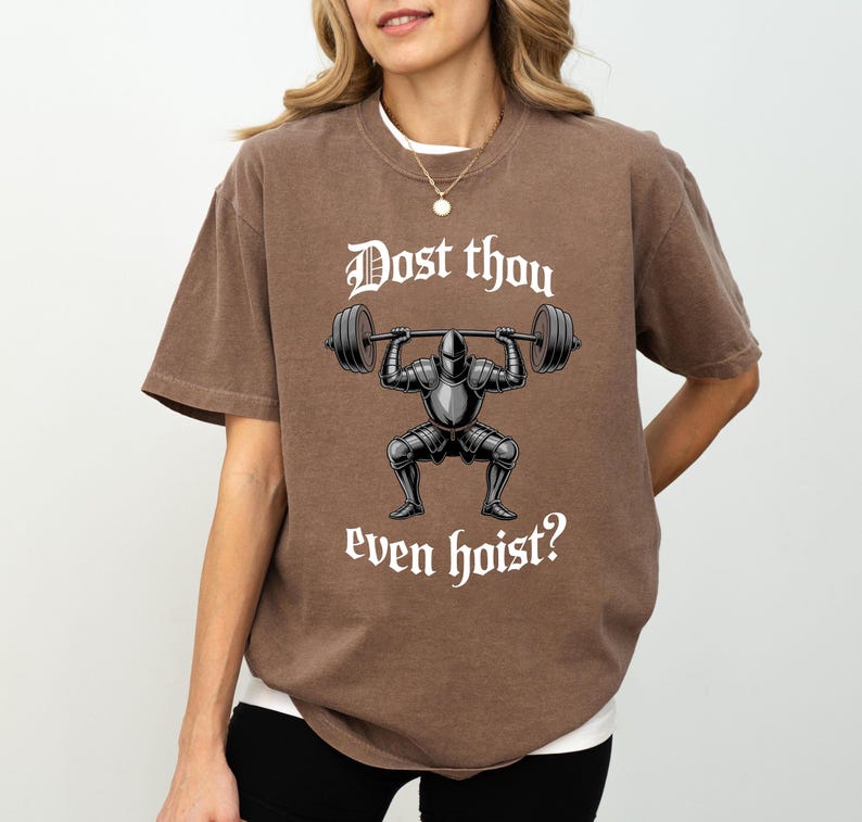May include: Brown t-shirt with the text "Dost thou even hoist?" above an illustration of a knight lifting weights. The knight is wearing armor and the barbell has weights on each end. The shirt has short sleeves.