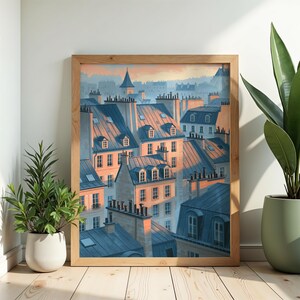 May include: A framed wall art print depicting a cityscape of multi-storey buildings with blue-grey pitched roofs and chimneys. The scene is illuminated by soft, warm golden light hitting the facades, creating a contrast with the cool blue shadows.