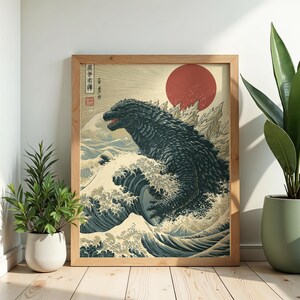 May include: A framed wall art print featuring a dark, textured monster rising from stylized blue ocean waves. A large red sun sits in the background above jagged mountain peaks. The artwork includes vertical Japanese text and a red square seal.