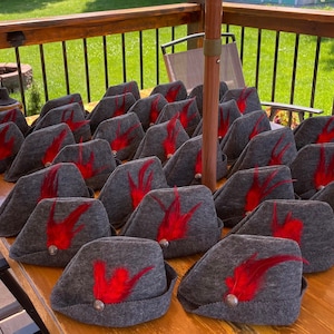 May include: A group of gray felt hats with red feather accents. The hats are arranged in rows on a wooden table.