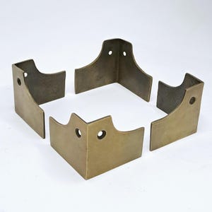 May include: Five antique brass corner braces. Each right-angled brace features a curved top and a single mounting hole. The brass has a warm, aged patina, indicating vintage or reclaimed materials. Ideal for furniture restoration.