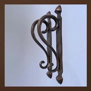 May include: A dark bronze-toned metal door knocker featuring a vertical mounting plate with pointed finials at the top and bottom. The swinging handle has a curved, scroll-like design that extends outward from the plate in a symmetrical shape.