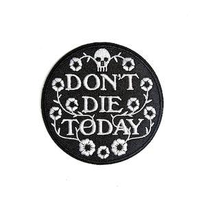 May include: A round, black embroidered patch with the words "DON'T DIE TODAY" in white, surrounded by white floral and vine designs. A white skull is at the top of the design.