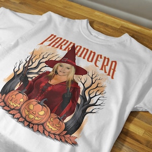 Puede incluir: Camiseta blanca con un diseño de Halloween. El diseño incluye una mujer con un disfraz de bruja, calabazas y el texto "PARRANDERA" en rojo. La ilustración tiene un estilo vintage e ilustrado.