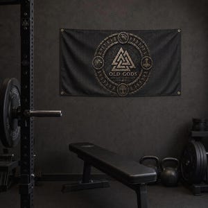 Könnte beinhalten: Ein rechteckiges schwarzes Wandbanner mit einem kreisförmigen Emblem, das ein zentrales Valknut-Symbol zeigt, umgeben von nordisch inspirierter Ikonografie und dem Text "OLD GODS STRENGTH PROJECT" in verwitterter Gold- und Bronzeoptik.