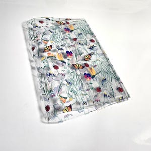 May include: A clear, rectangular, floral-patterned item featuring butterflies, ladybugs, and various flowers in shades of yellow, orange, purple, and green. The item is folded and appears to be made of a transparent material.