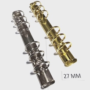 Op de afbeelding: Twee metalen ringbanden, één zilverkleurig en één goudkleurig, worden getoond op een wit oppervlak. De gouden ringband zit rechts en de zilveren links. De tekst "27 mm" is zichtbaar.