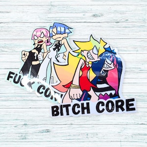 Könnte beinhalten: Zwei Aufkleber mit Anime-Charakteren. Einer trägt den Text "FUCK CORE" und der andere "BITCH CORE". Die Charaktere haben rosa, blaue und gelbe Haare und tragen Outfits in Schwarz, Weiß und Rot. Auf einer Holzoberfläche.
