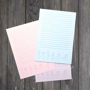 May include: Pink and blue lined stationery sheets with a whimsical illustration of dancing figures. The stationery has a gradient color scheme and is suitable for writing letters or notes.