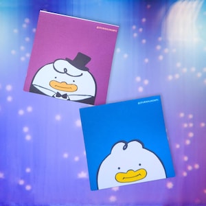 Puede incluir: Dos cuadernos cuadrados con ilustraciones de patos de dibujos animados. Uno es morado con un pato con esmoquin y sombrero de copa. El otro es azul con una ilustración de pato. El texto "#JOURNALINGNCFC" está impreso en ambos cuadernos.