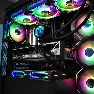 May include: A computer tower with multiple fans illuminated with rainbow LED lights. The graphics card reads "GEFORCE RTX". The fans and lights are arranged throughout the interior of the computer case.