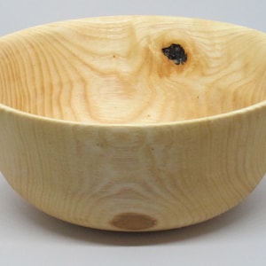 Könnte beinhalten: Eine große, helle Holzschale mit natürlicher Oberfläche. Die Schale hat eine glatte, abgerundete Form und einen leicht ausgestellten Rand. Die Holzmaserung ist in der gesamten Schale sichtbar.
