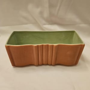 May include: A rectangular planter with a light brown exterior and a green interior. The planter has a wavy design on the sides. The interior is a light green color. The planter is empty.