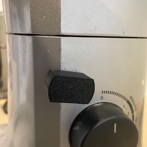 May include: Close-up of a silver and grey stand mixer with a black knob and a textured black handle. The mixer has a dial with numbers and the words "Knead & Pulse."