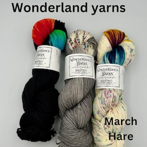 May include: Three skeins of yarn in black, gray, and white with colorful flecks. The yarn is labeled "Wonderland Yarns" and "March Hare".